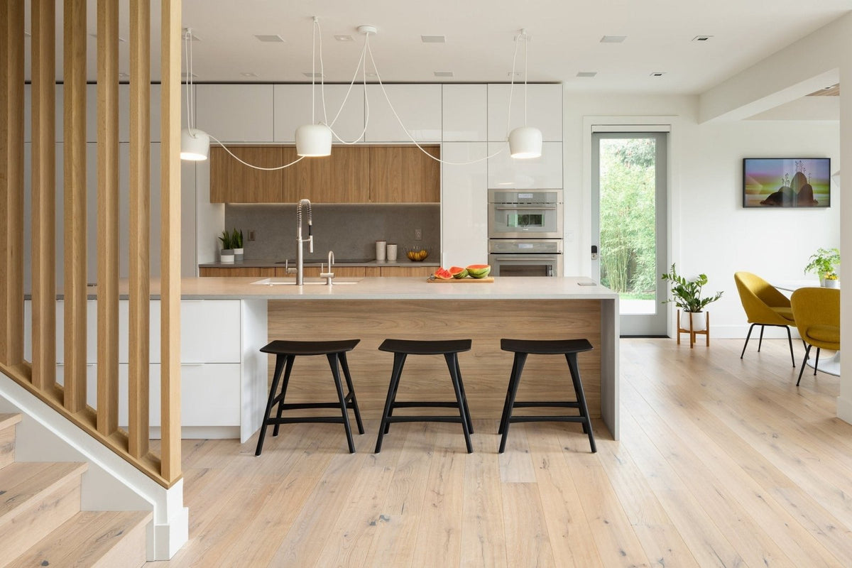 Modern kitchen island with light wood engineered wood flooring countertop and white cabinetry with three black bar stools