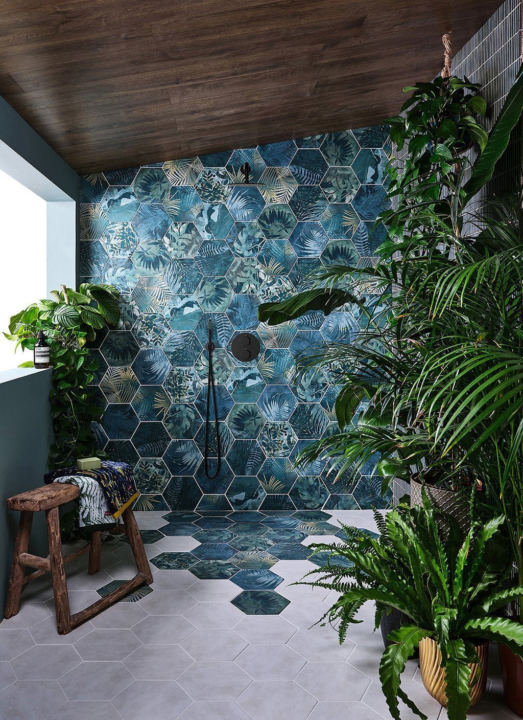 Hexagonal shower wall tiles with tropical leaf pattern in shades of teal and green for stylish bathroom decor