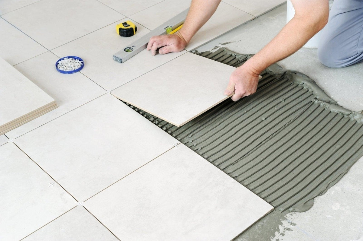 Light gray rectangular ceramic floor tile being installed with adhesive in a how to remove ceramic floor tiles article