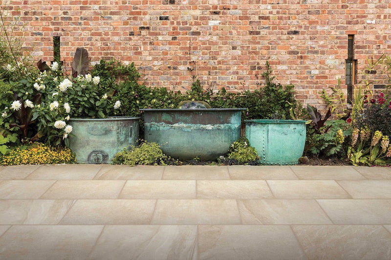 Three weathered copper planters with verdigris patina arranged against a brick wall in a patio setting with porcelain tiles