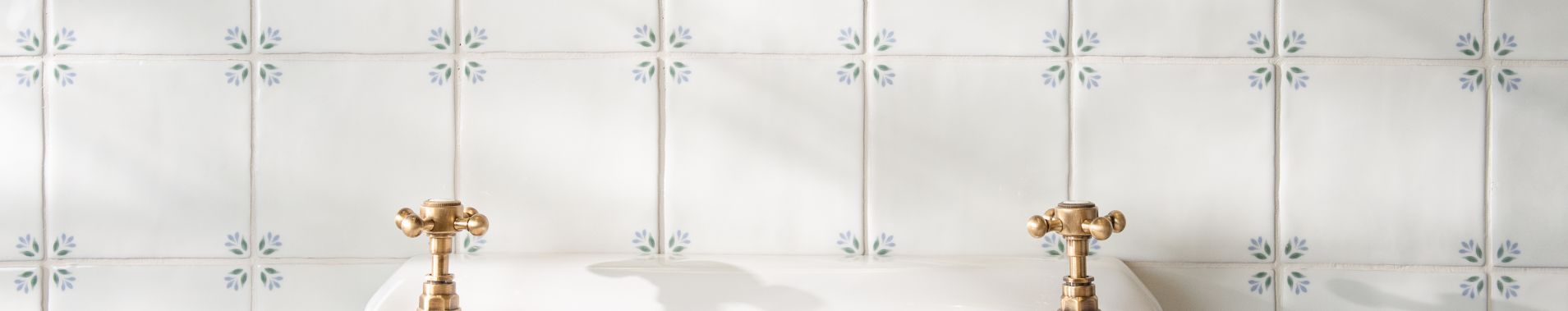 Gold-toned ornate faucet handles with intricate detailing on a white tiled surface from original style spring tiles collection