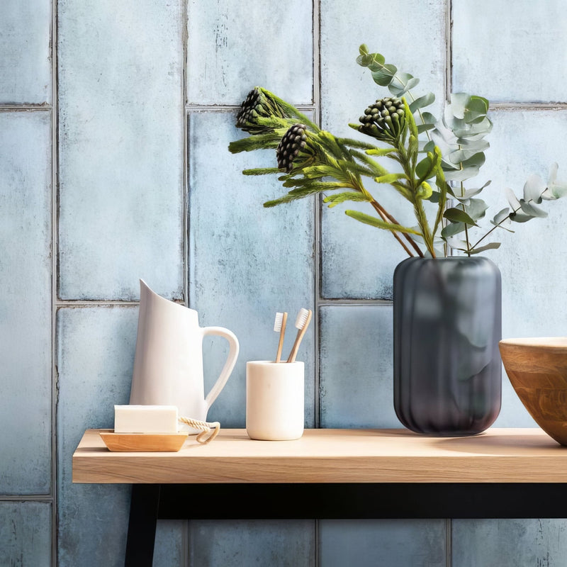 Dark gray textured glass vase holding green eucalyptus and dark spiky flowers from the blue tiles collection
