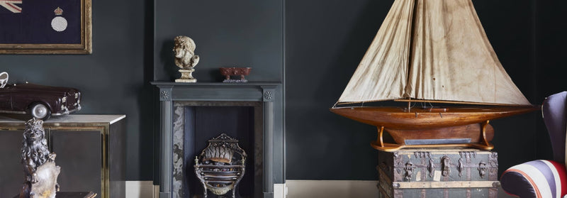 A detailed wooden model sailboat with beige fabric sail resting on an ornate metal trunk from dark paint collection