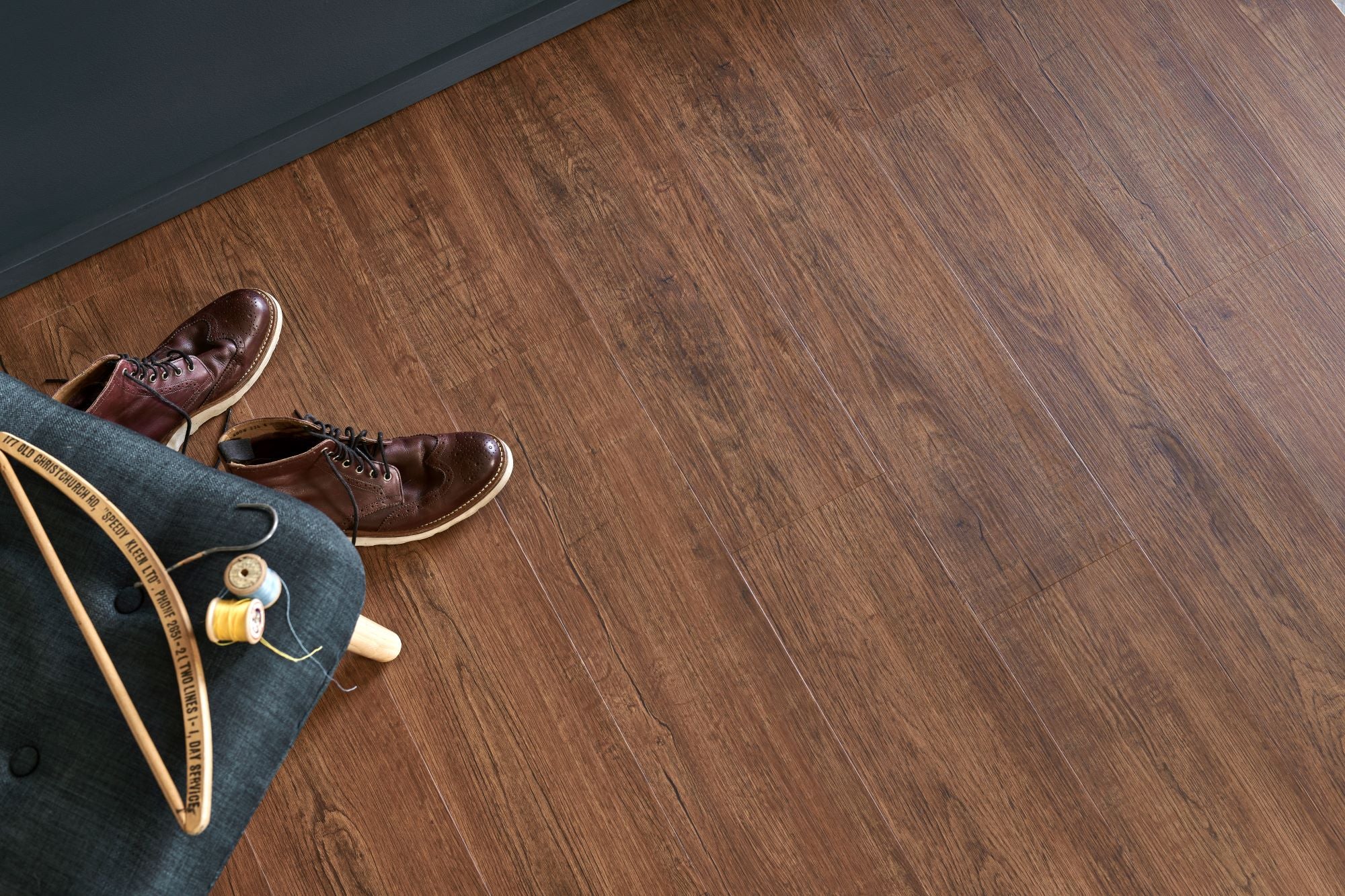 Brown leather lace-up shoes with light-colored sole on engineered wood flooring next to denim fabric and sewing supplies