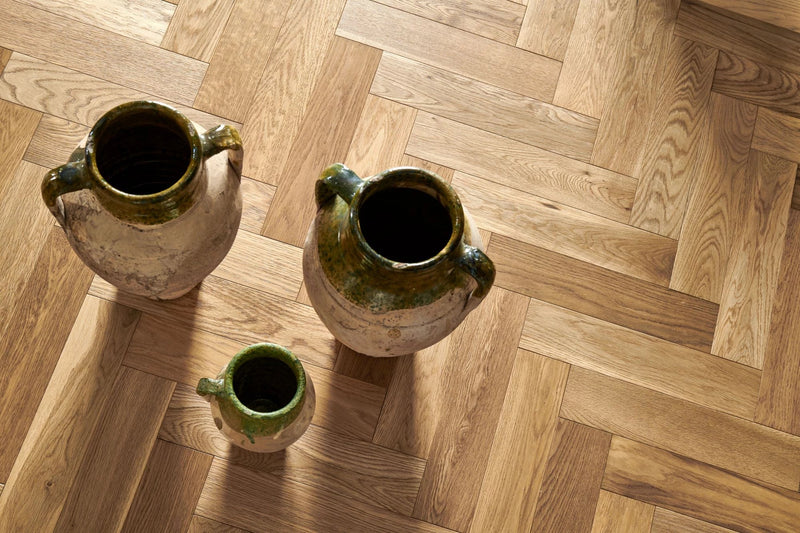 Three rustic ceramic jugs with green glazed rims and handles on herringbone wood flooring
