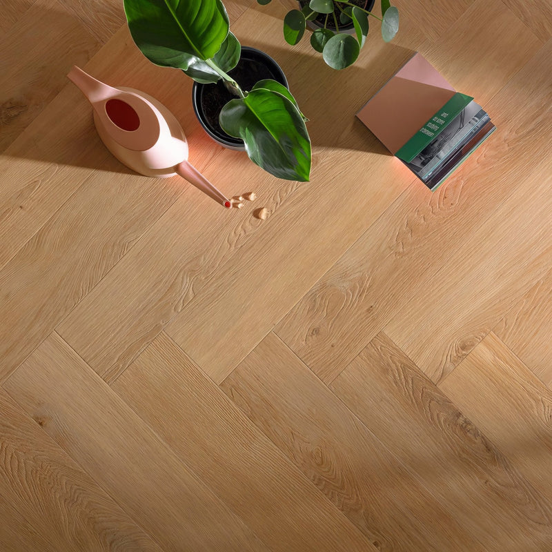 Light oak-colored hardwood floor with a herringbone pattern from luxury herringbone LVT rigid core parquet collections