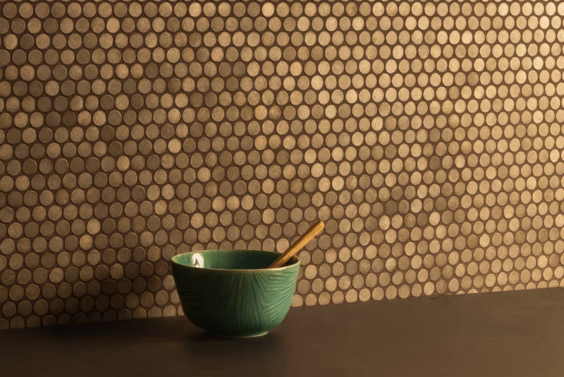A teal ceramic bowl with subtle texture resting on a dark surface against metallic gold penny mosaic tiles backdrop