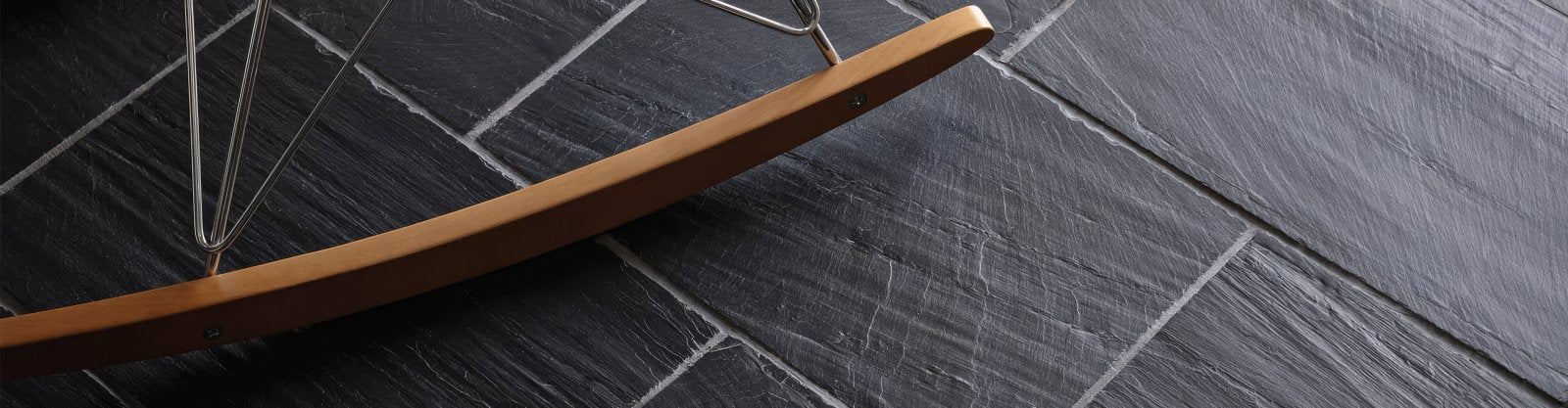 A sleek curved wooden beam with a smooth finish resting on dark gray slate tiles from the slate tiles collection