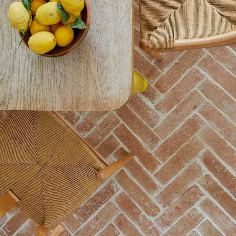 A wooden bowl filled with bright yellow lemons with green leaves in a terracotta tiles collection