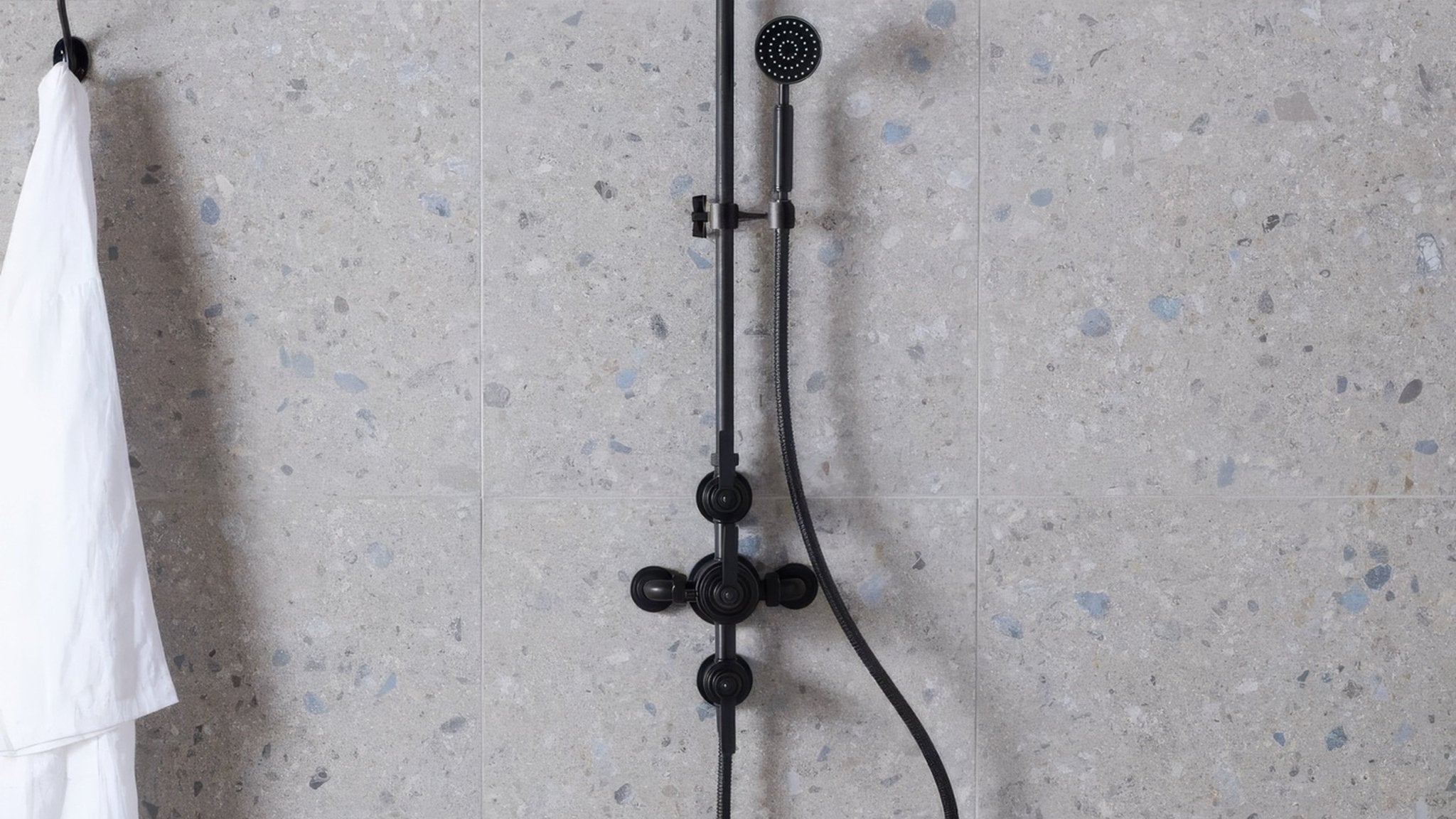 Black matte-finished shower system with modern design and adjustable handheld nozzle in terrazzo effect wall tiles collection
