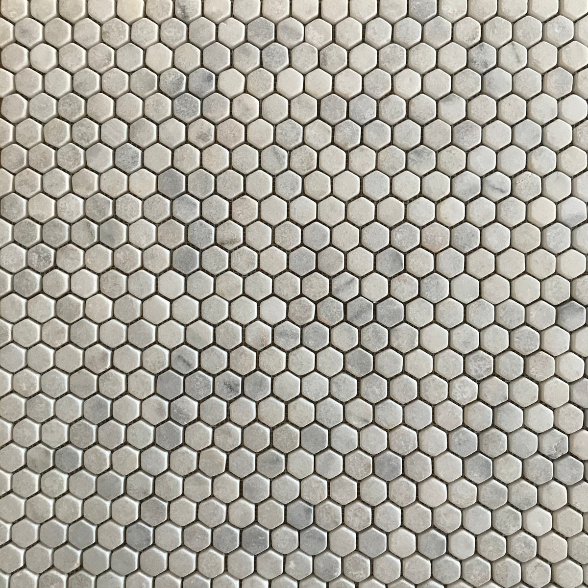 Close detail of tumbled Carrara marble hexagons showing rounded edges and a matt, faintly pitted face