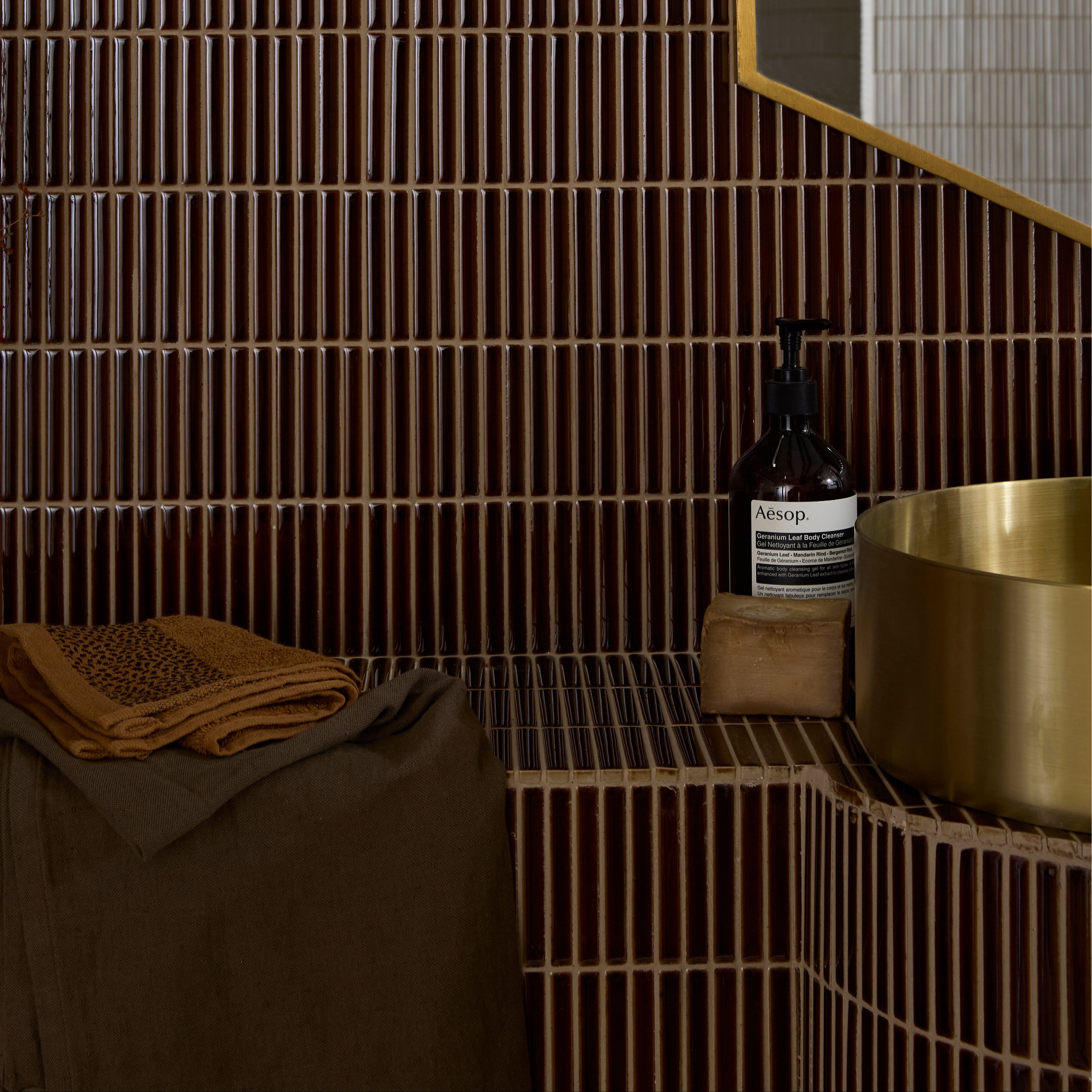 Bathroom setting with a gold bowl, towel, and bottles on a tiled shelf.