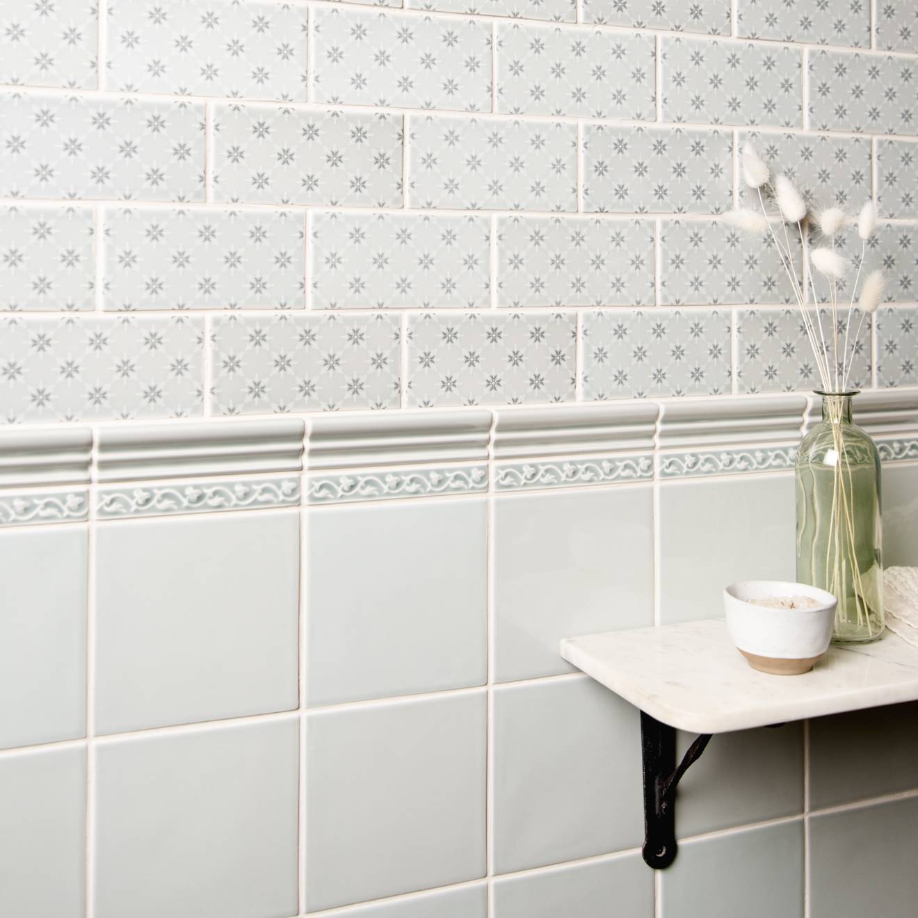 White subway tile wall with gray floral pattern and decorative border from beaulieu moulding sudbury collection