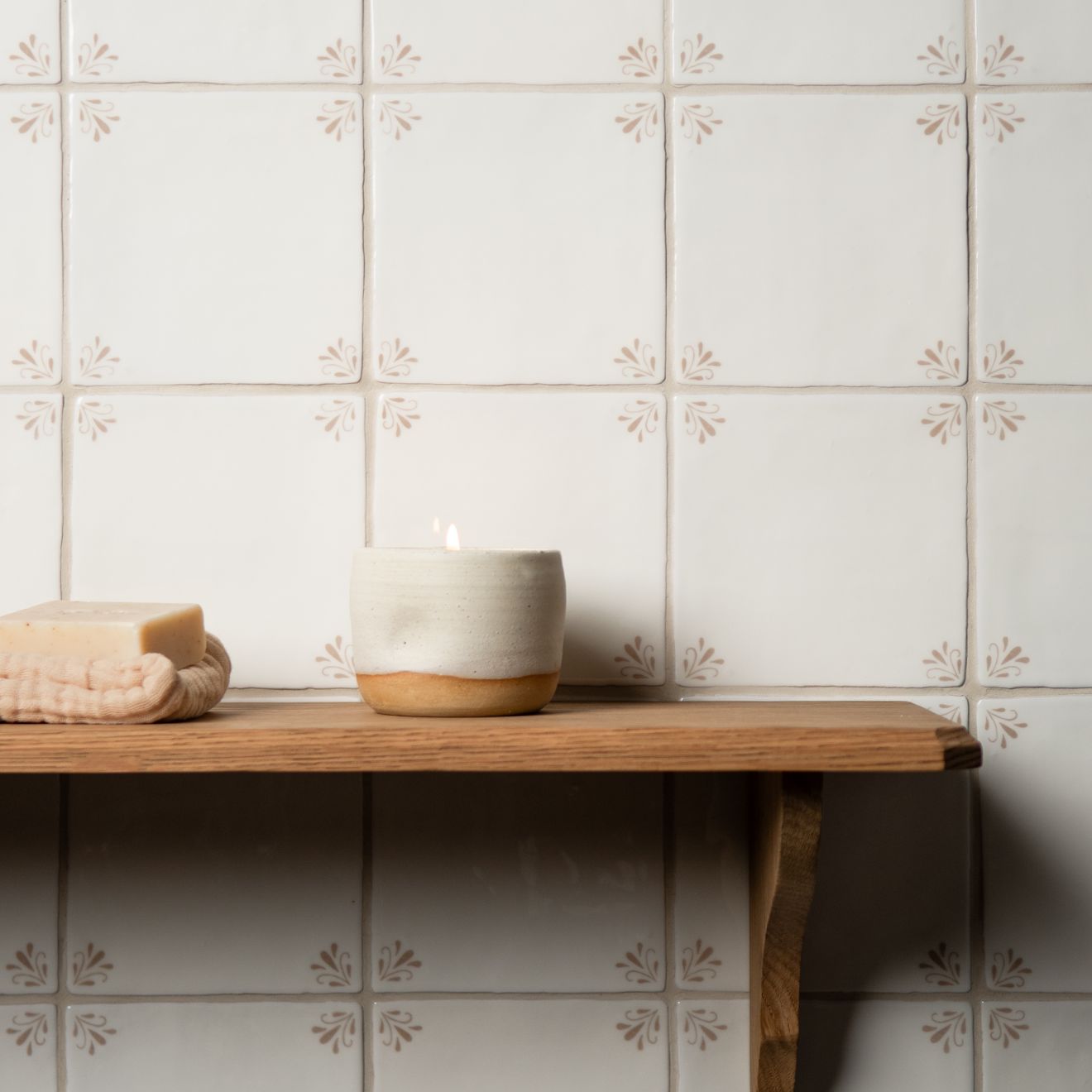 Candle and soap on a wooden shelf against a tiled wall