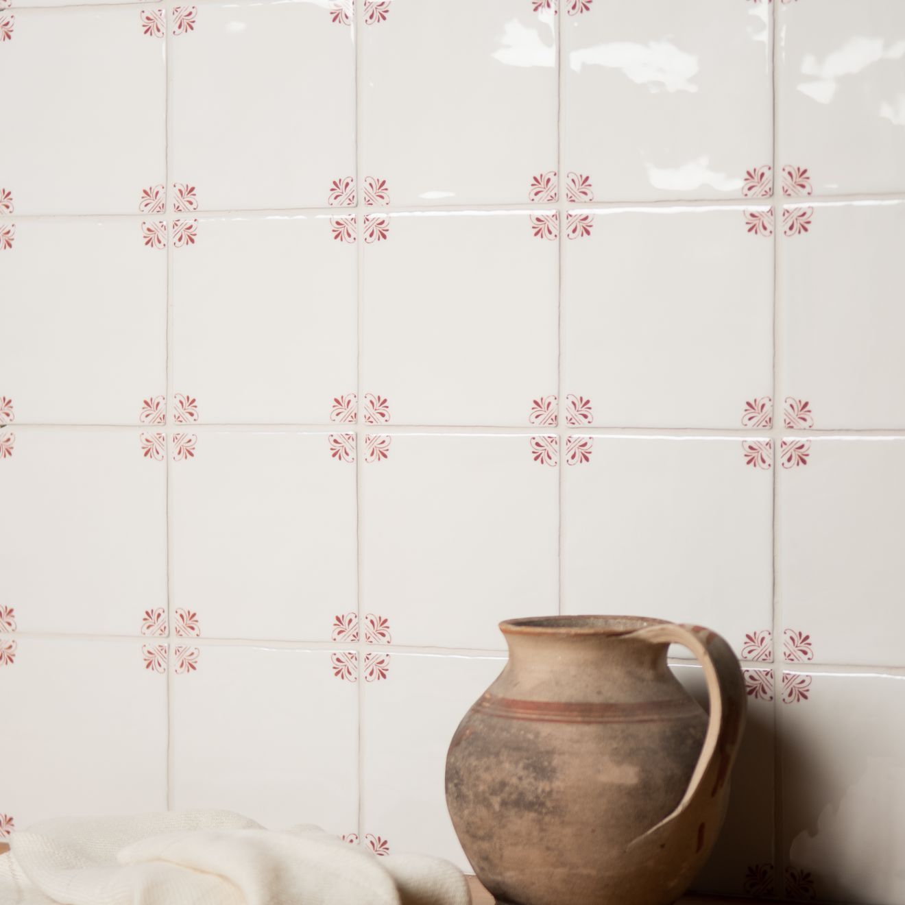 Brown ceramic pitcher against a tiled wall with decorative patterns