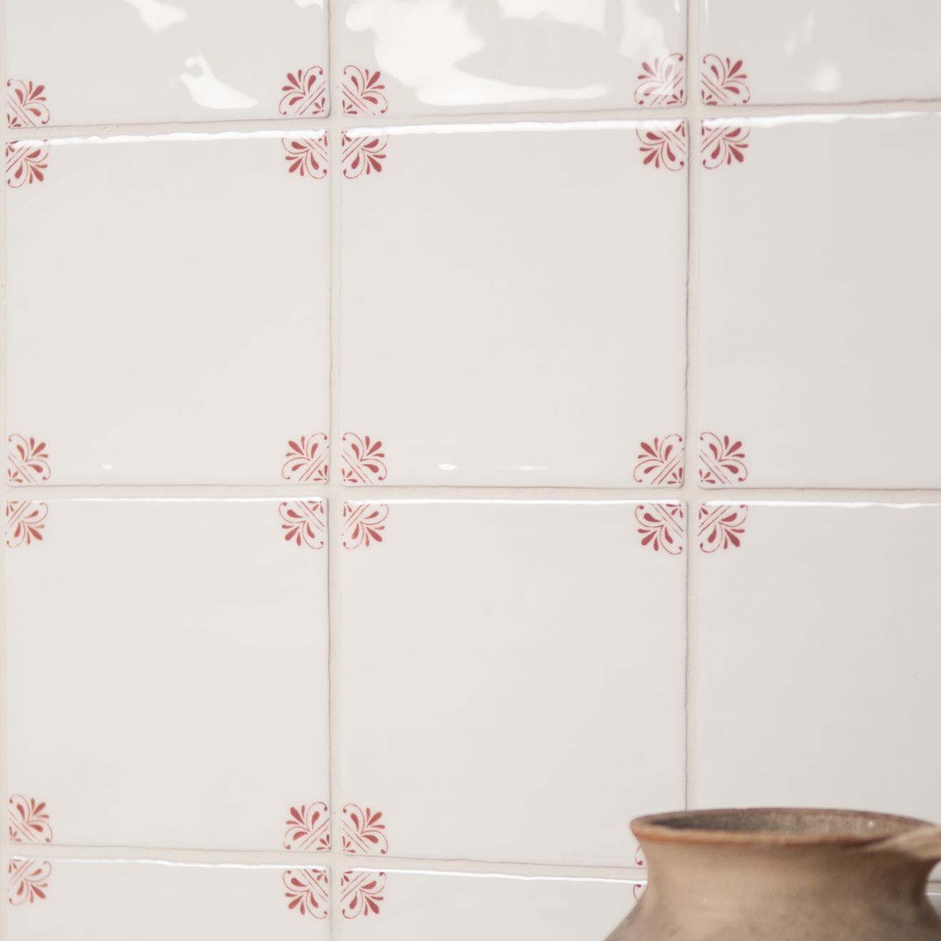 White tiles with red floral patterns on a wall with a ceramic pot in the corner.