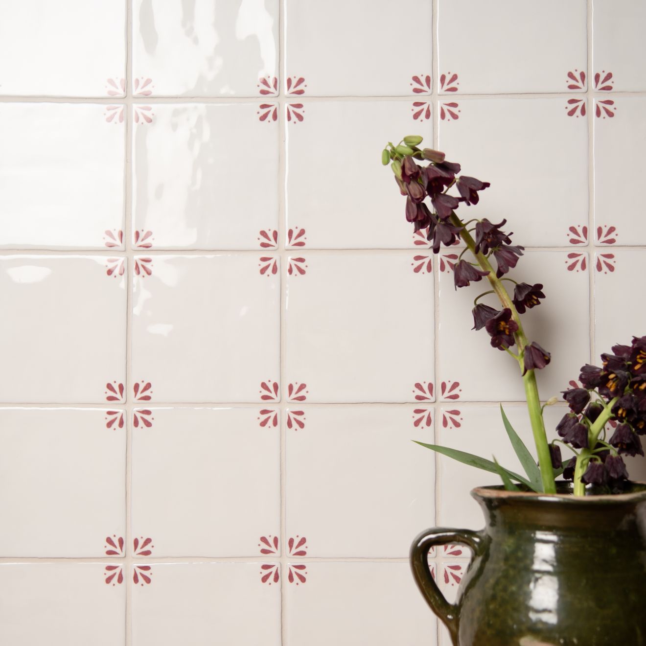 Decorative tiles with a floral pattern on a white wall with a vase of flowers.