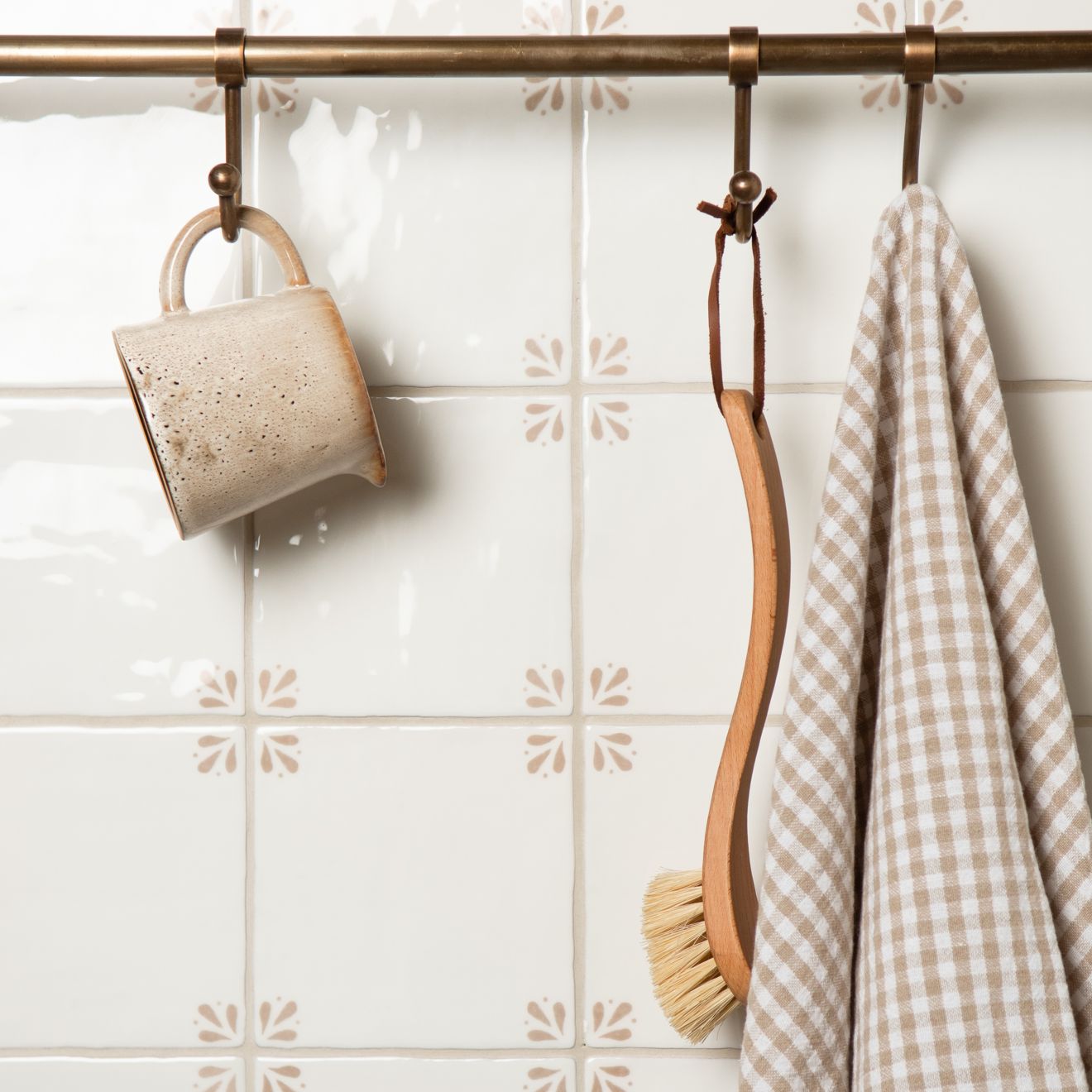 Ceramic mug, wooden spoon, and checkered towel hanging on a rack against a tiled wall.