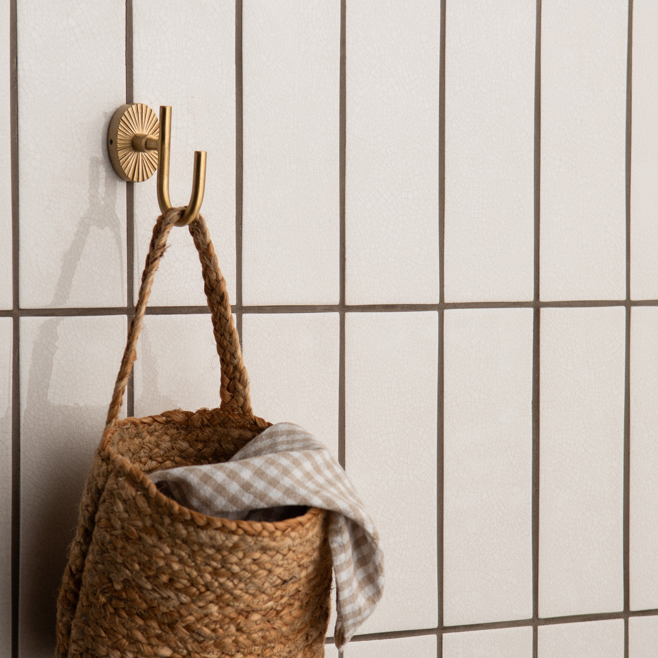 A woven jute basket with braided handles hanging from a brass sunburst hook showcasing crackle glazed brick tile helmingham
