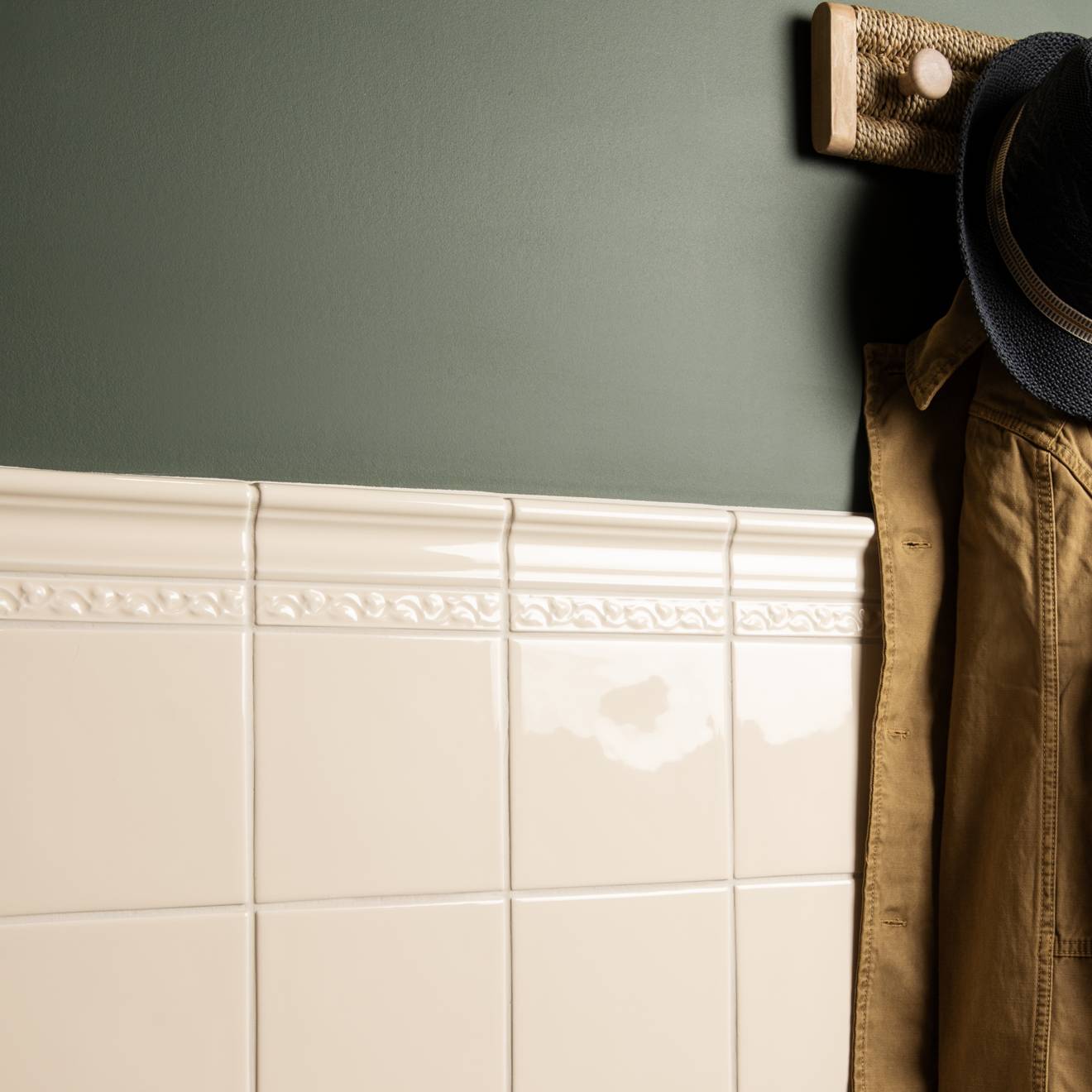 Brown jacket hanging on a wooden hook against a green wall with white tiled wall.