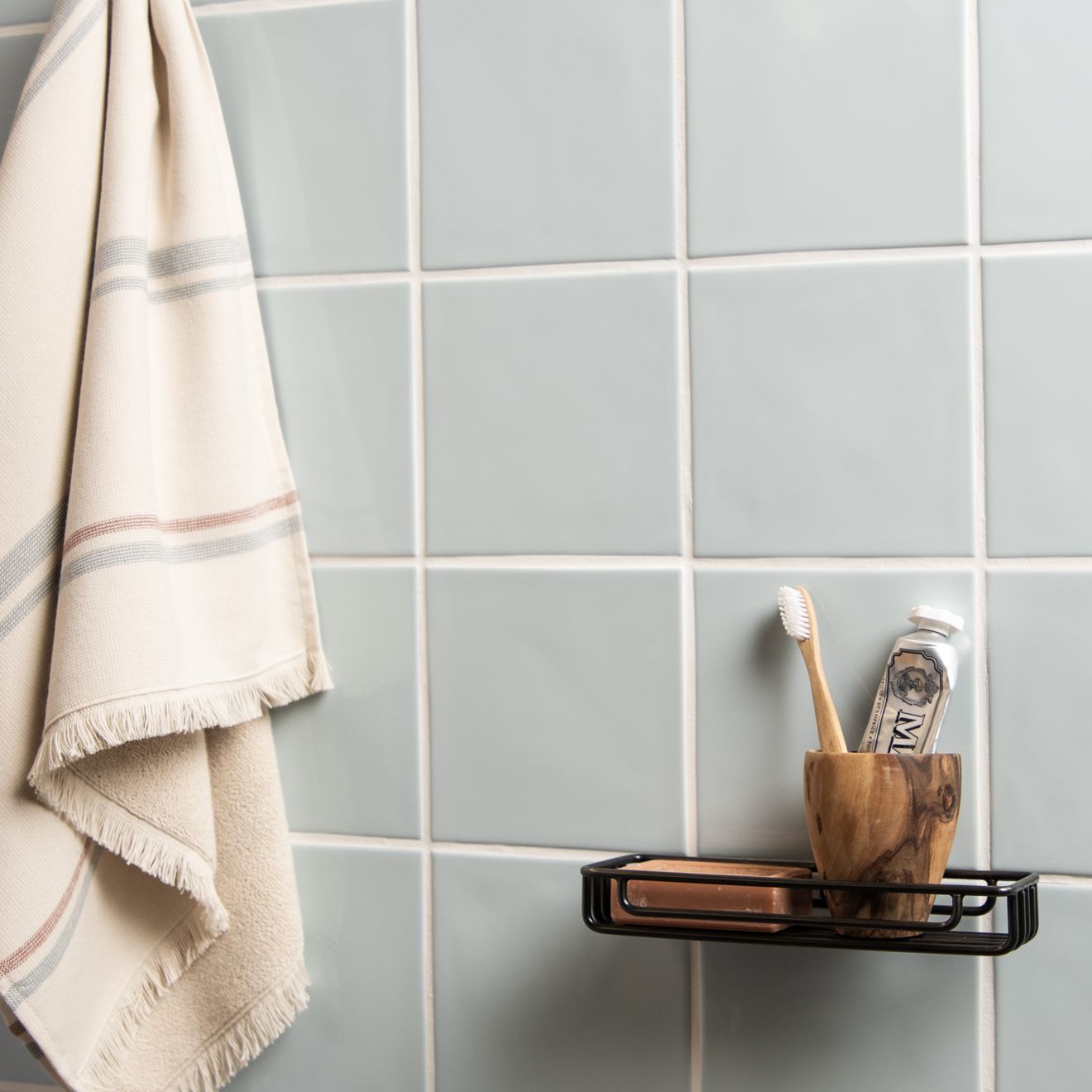 Bathroom setting with a towel hanging on a rack and toiletries on a shelf against a tiled wall.