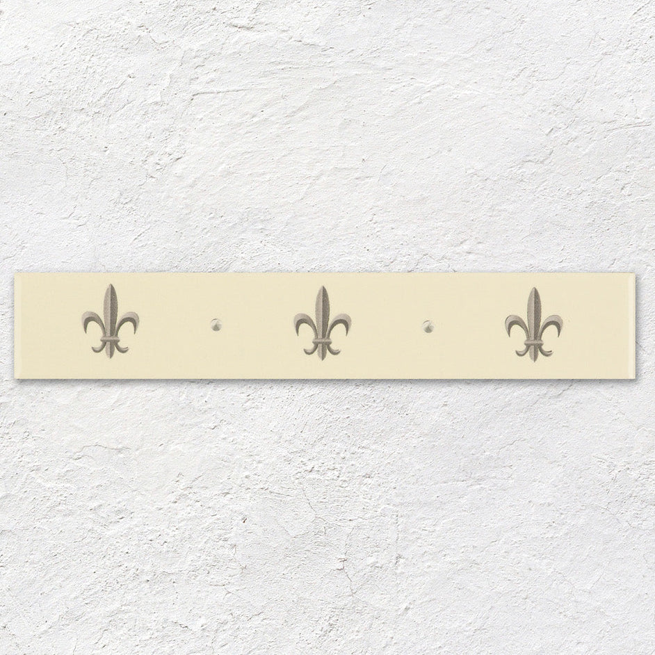 Cream-colored rectangular wall-mounted coat rack with three metallic fleur de lis hooks in platinum on county white