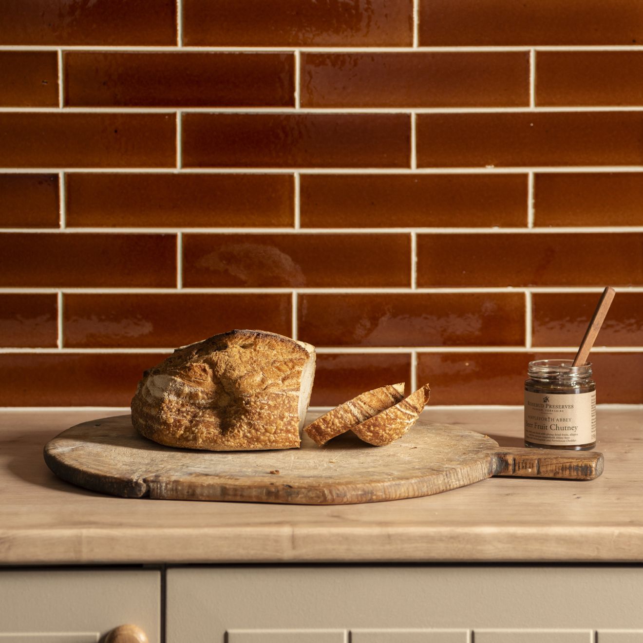 A rustic round wooden cutting board with artisanal sourdough bread on a moor brick tile surface