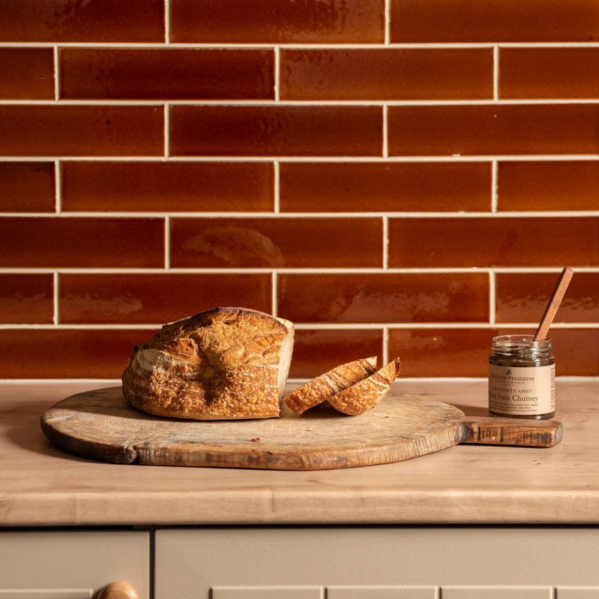 A rustic round wooden cutting board with artisanal sourdough bread on a moor brick tile surface