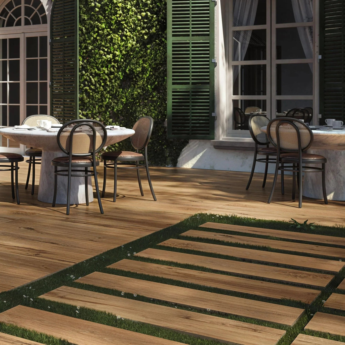 Outdoor dining area with tables and chairs on a wooden deck, greenery, and building in the background.