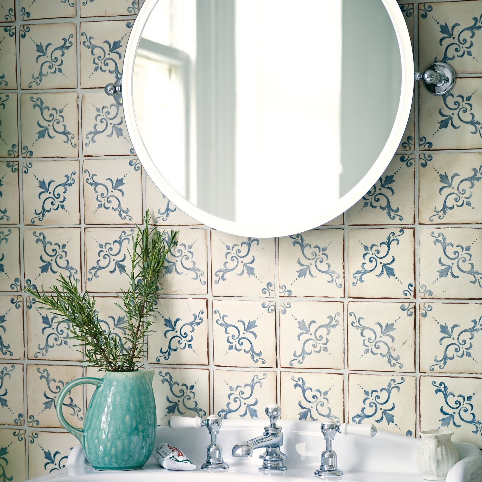 A teal ceramic pitcher with a textured surface and handle holding fresh rosemary for paris isabelle patterned terracotta tile decor