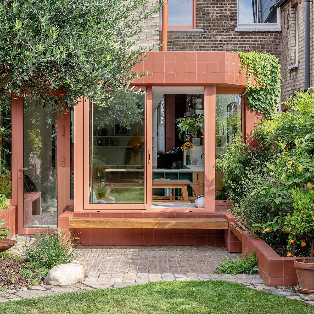 A modern sunroom featuring quarry red square terracotta tiles with large glass windows and wooden bench seating
