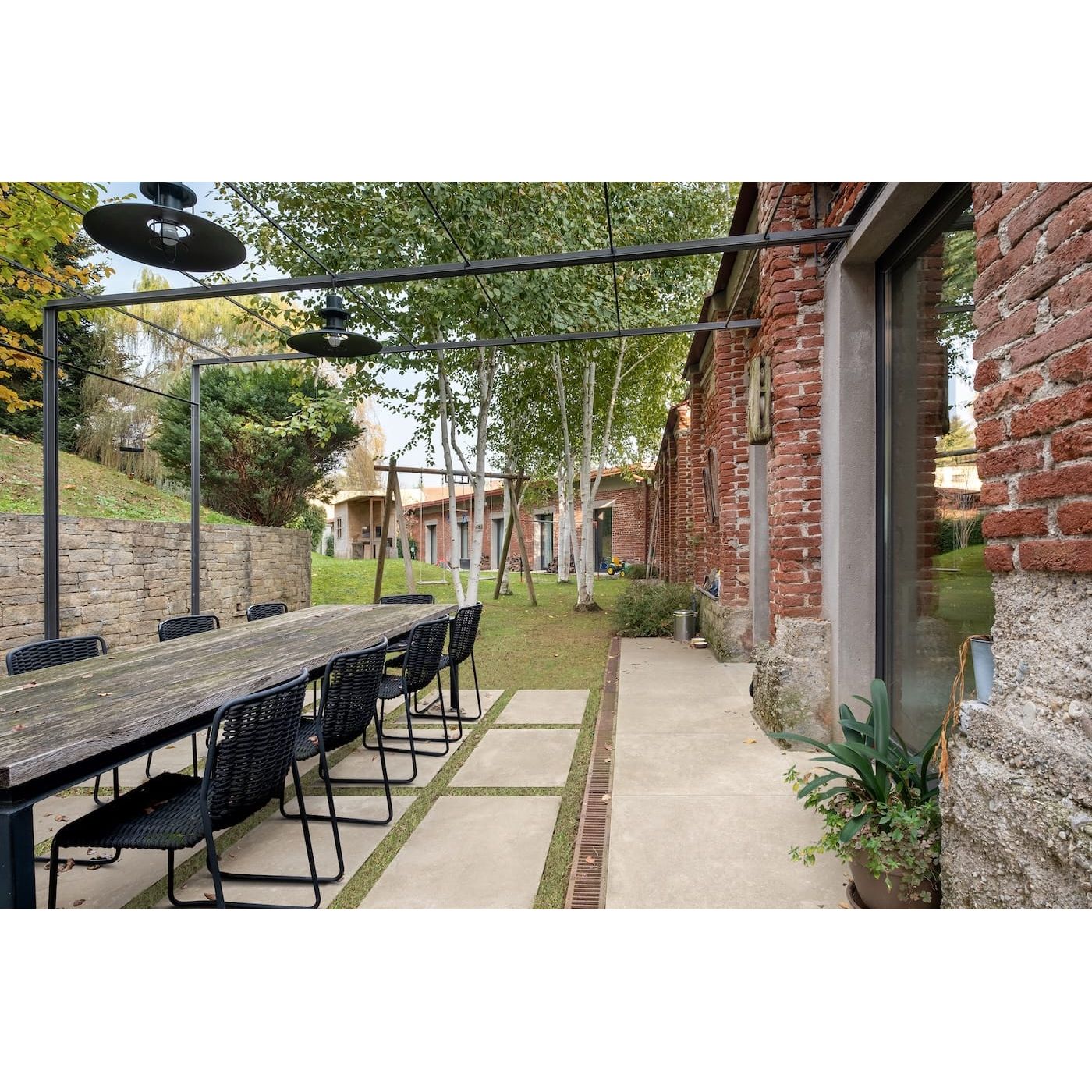 Outdoor dining area with long wooden table and chairs near a brick building.