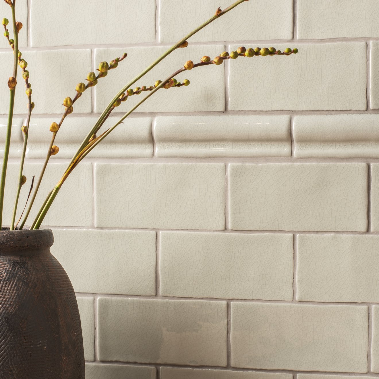 Dark textured ceramic vase torus moulding tern holding slender green stems with budding yellow flowers