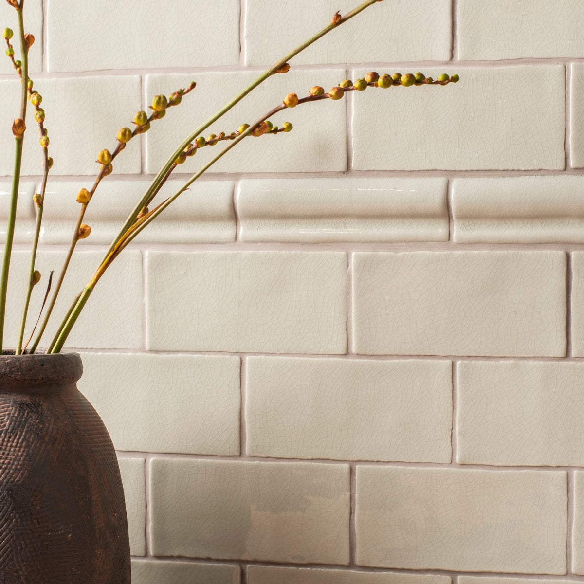 Dark textured ceramic vase torus moulding tern holding slender green stems with budding yellow flowers