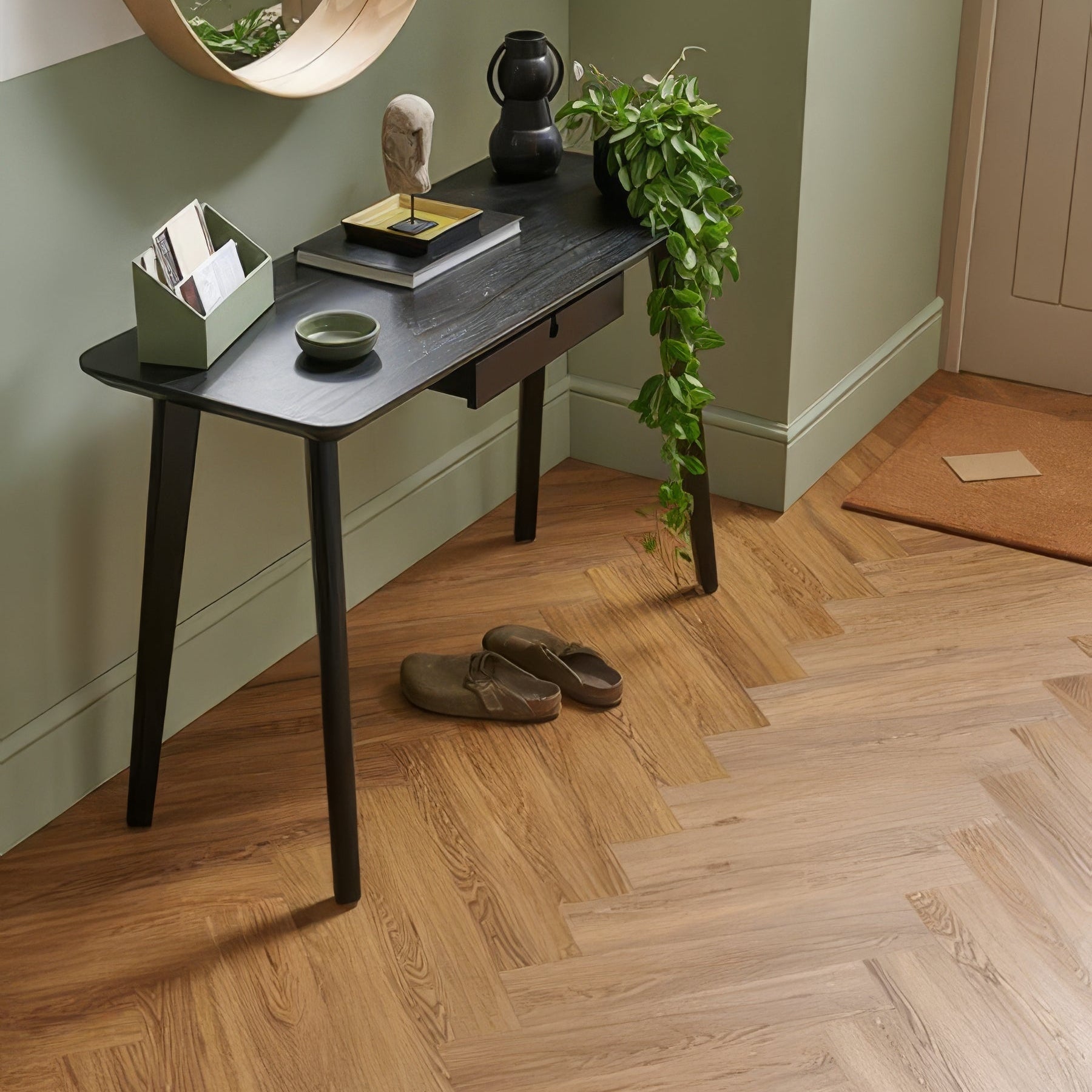 Small black console table against a green wall with a mirror above it, on a Woodpecker Weymouth Millhouse Oak Herringbone.