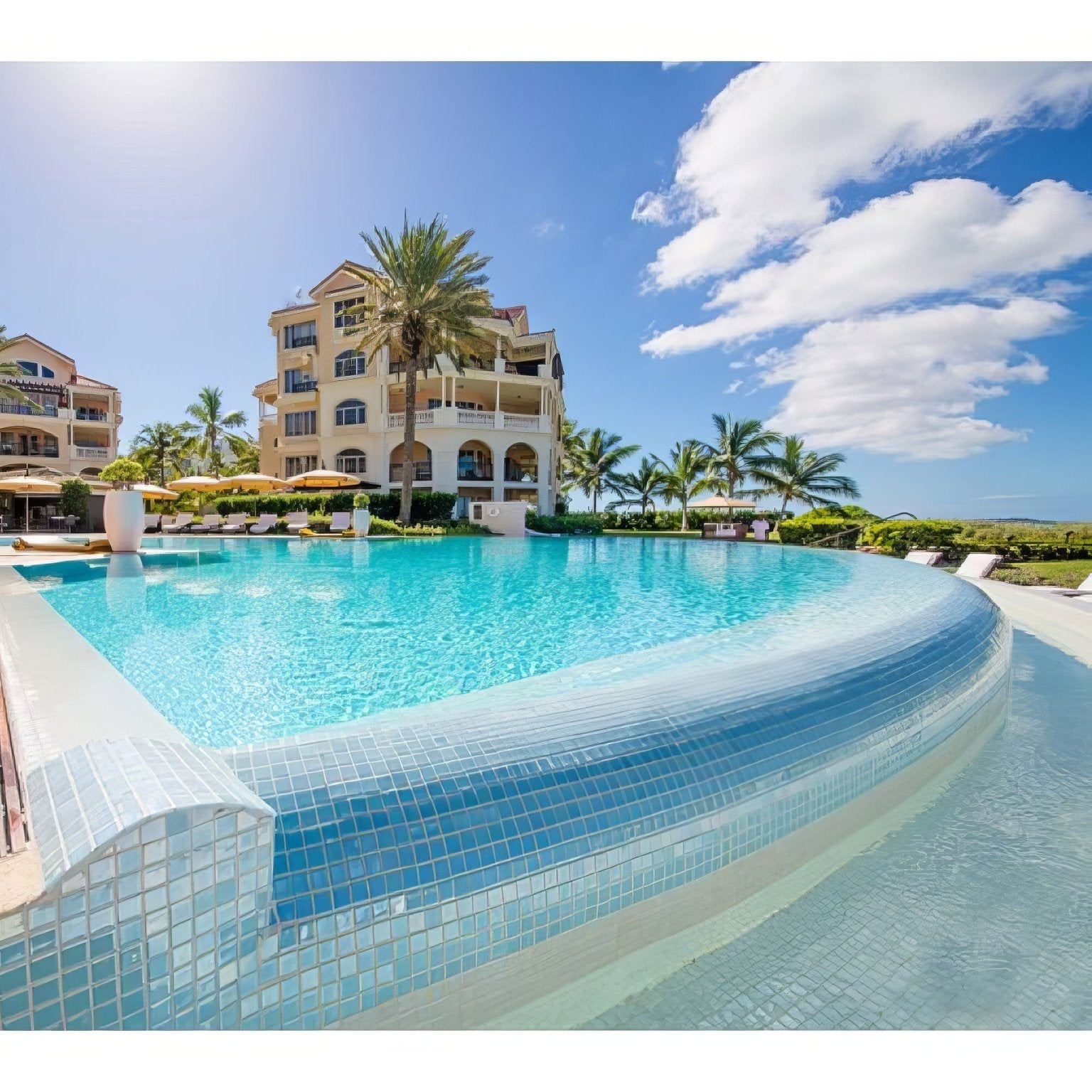A curved swimming pool with abalone ocean iridescent turquoise glass mosaic tiles and a white tiled edge