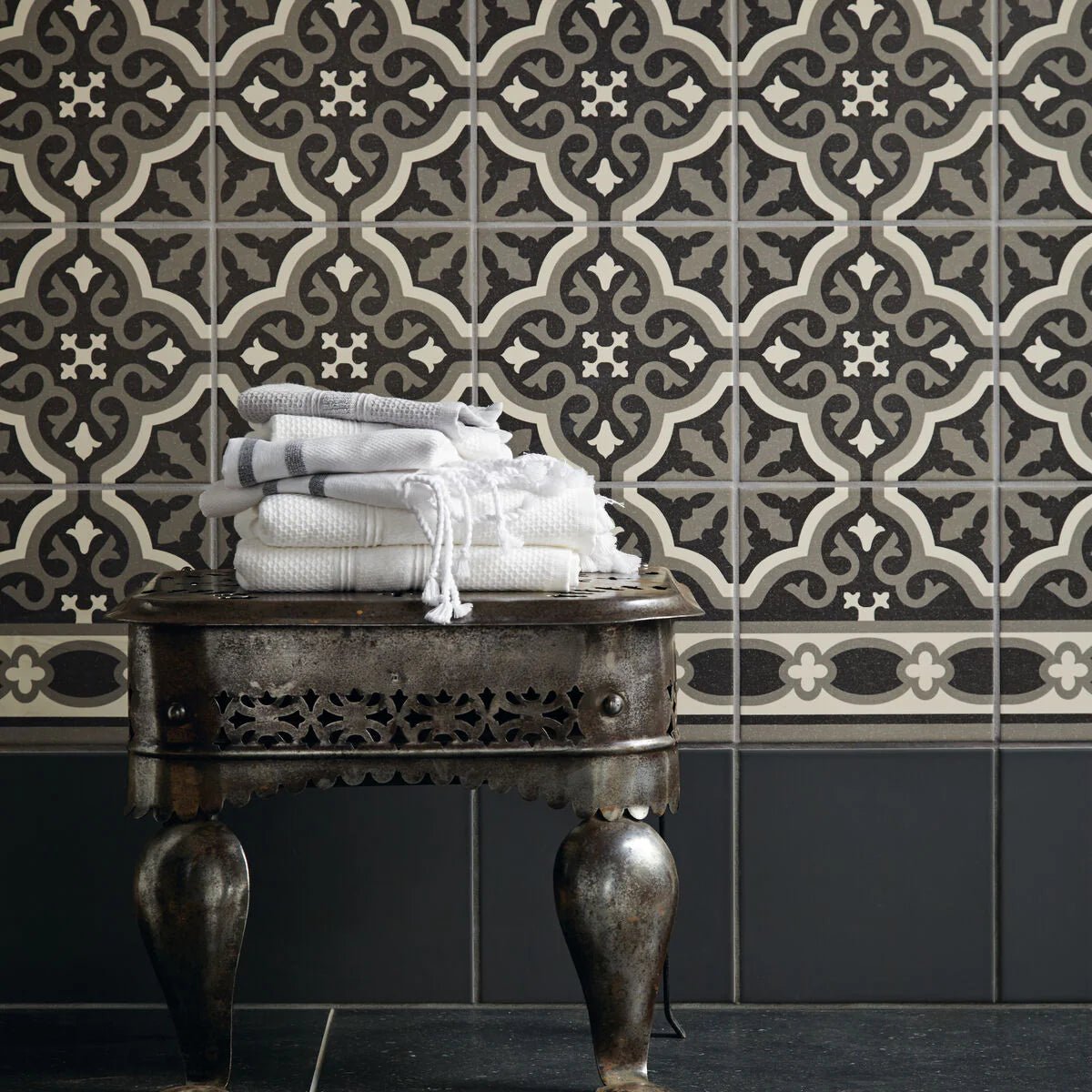 Stack of white and gray textured towels with fringed edges on ornate metal table for abbey waverley border tile