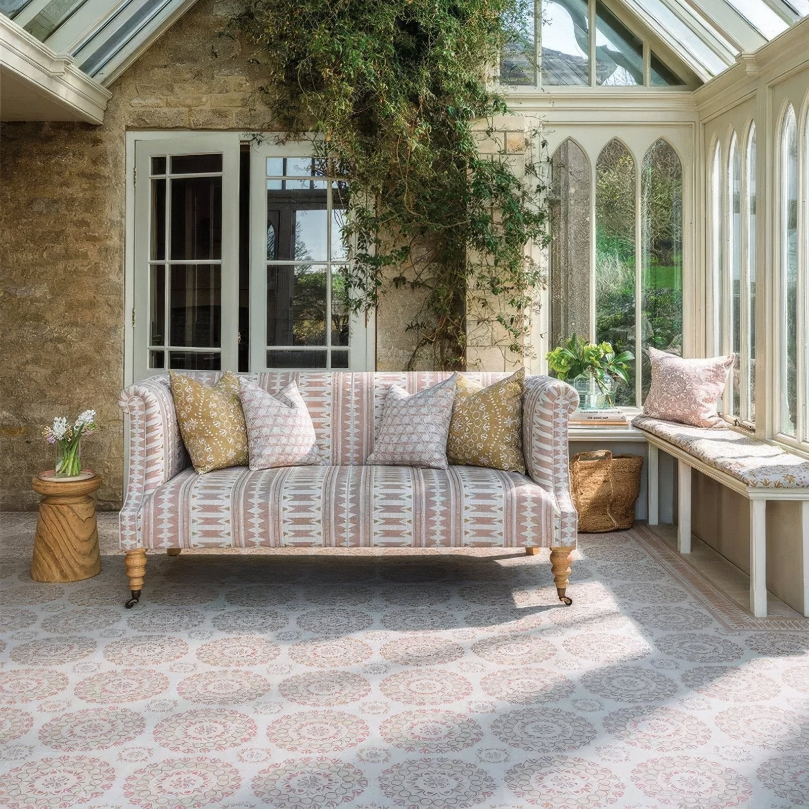 A plush upholstered sofa with soft pink and beige geometric fabric wooden legs and decorative throw pillows in terracotta tones