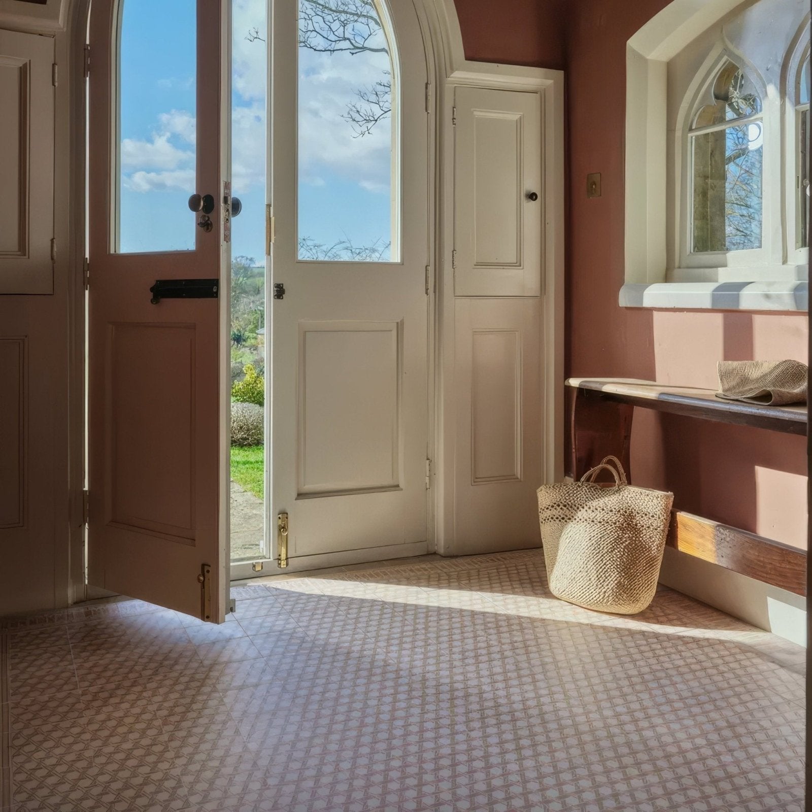 A woven straw tote bag with sturdy handles in natural light beige resting near an open doorway with terracotta decor