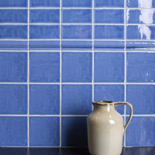 Cream-colored ceramic pitcher with curved handle and spout against agapanthus field tile blue backdrop