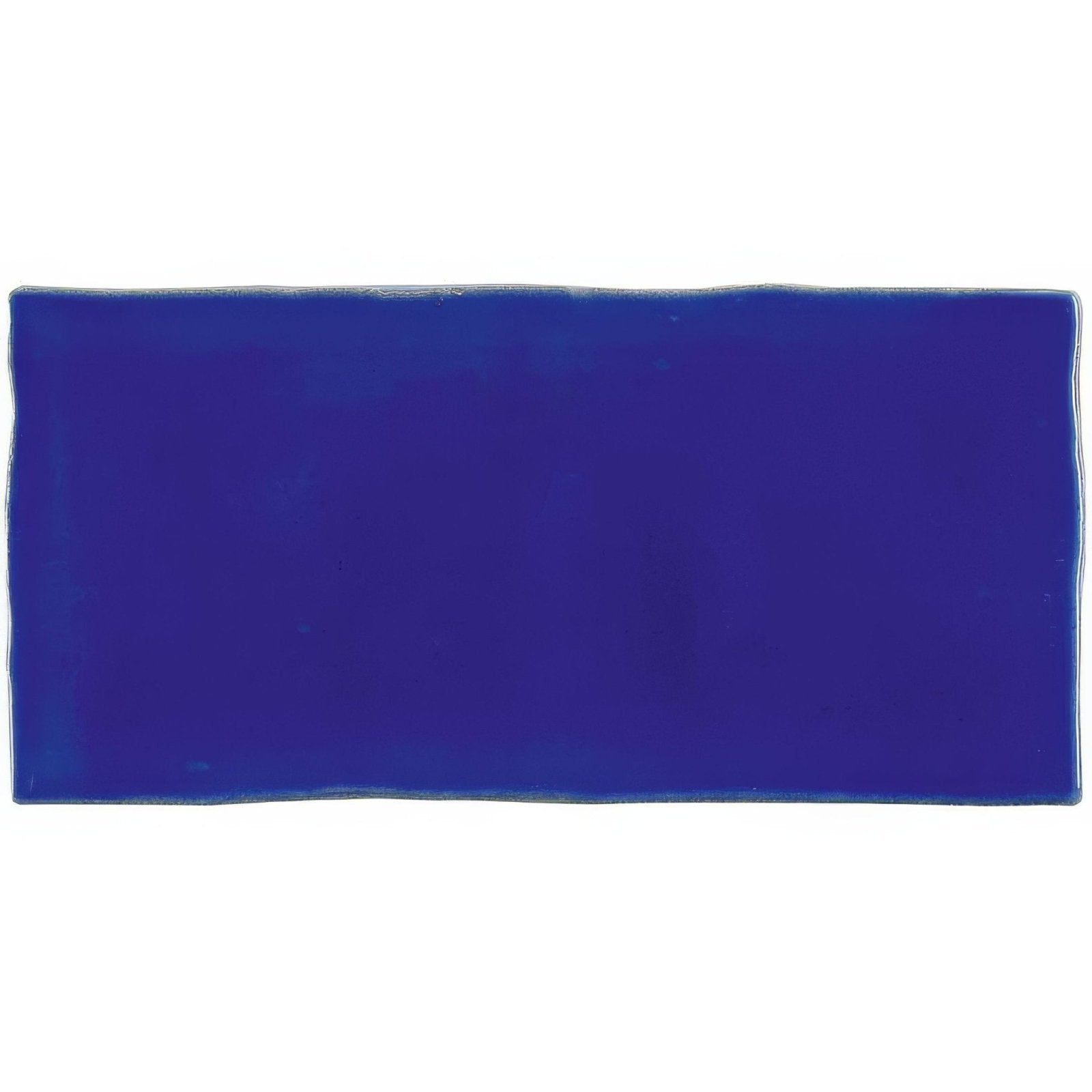A glossy royal blue rectangular amun half tile wall tile with slightly uneven wavy edges for wall decor