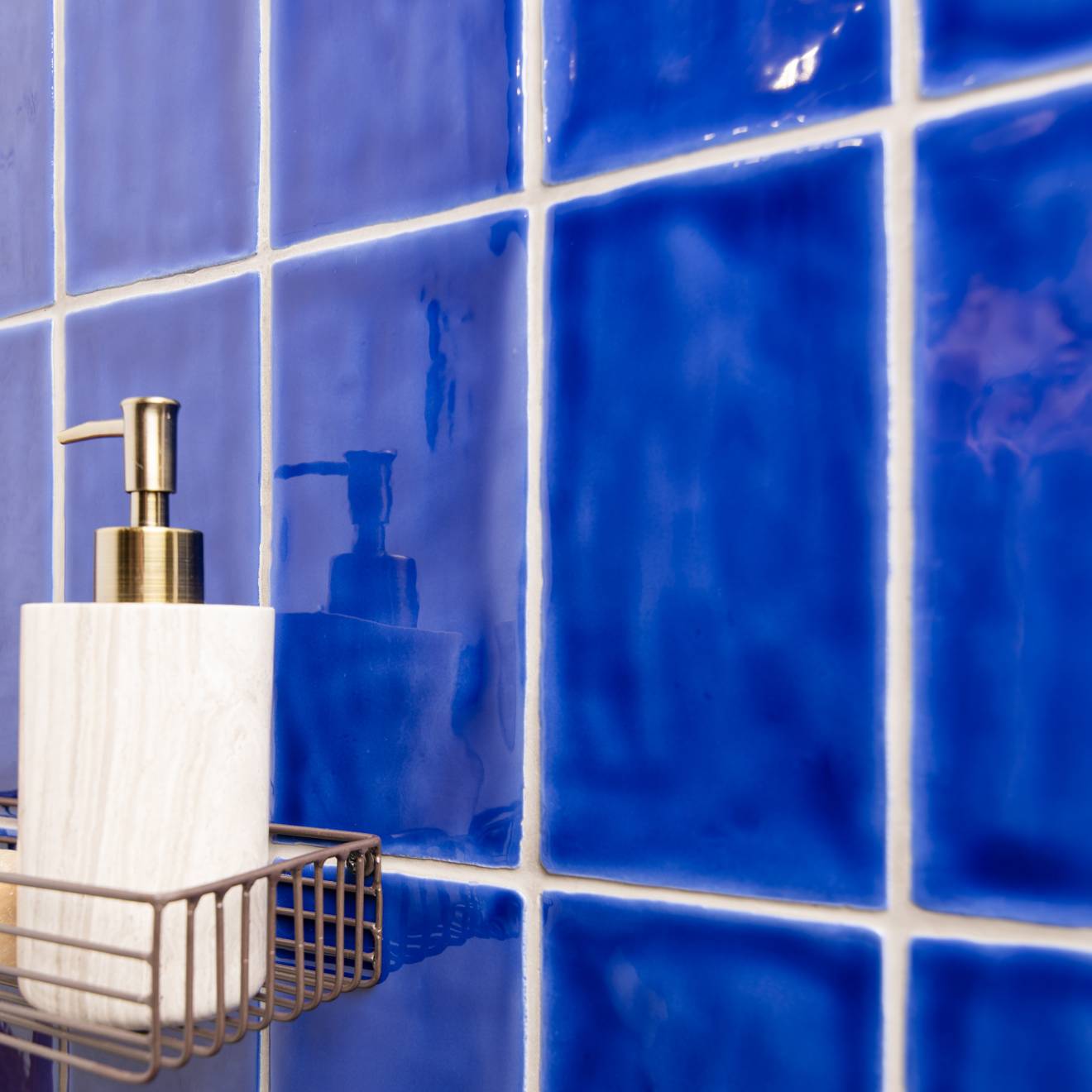 A white marble soap dispenser with a gold-tone pump in a wire rack against amun half tile blue wall tiles