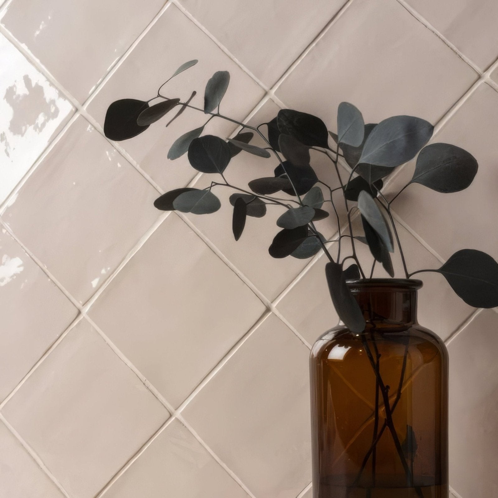 A dark amber glass bottle with eucalyptus branches paired with anemone field tile decor element