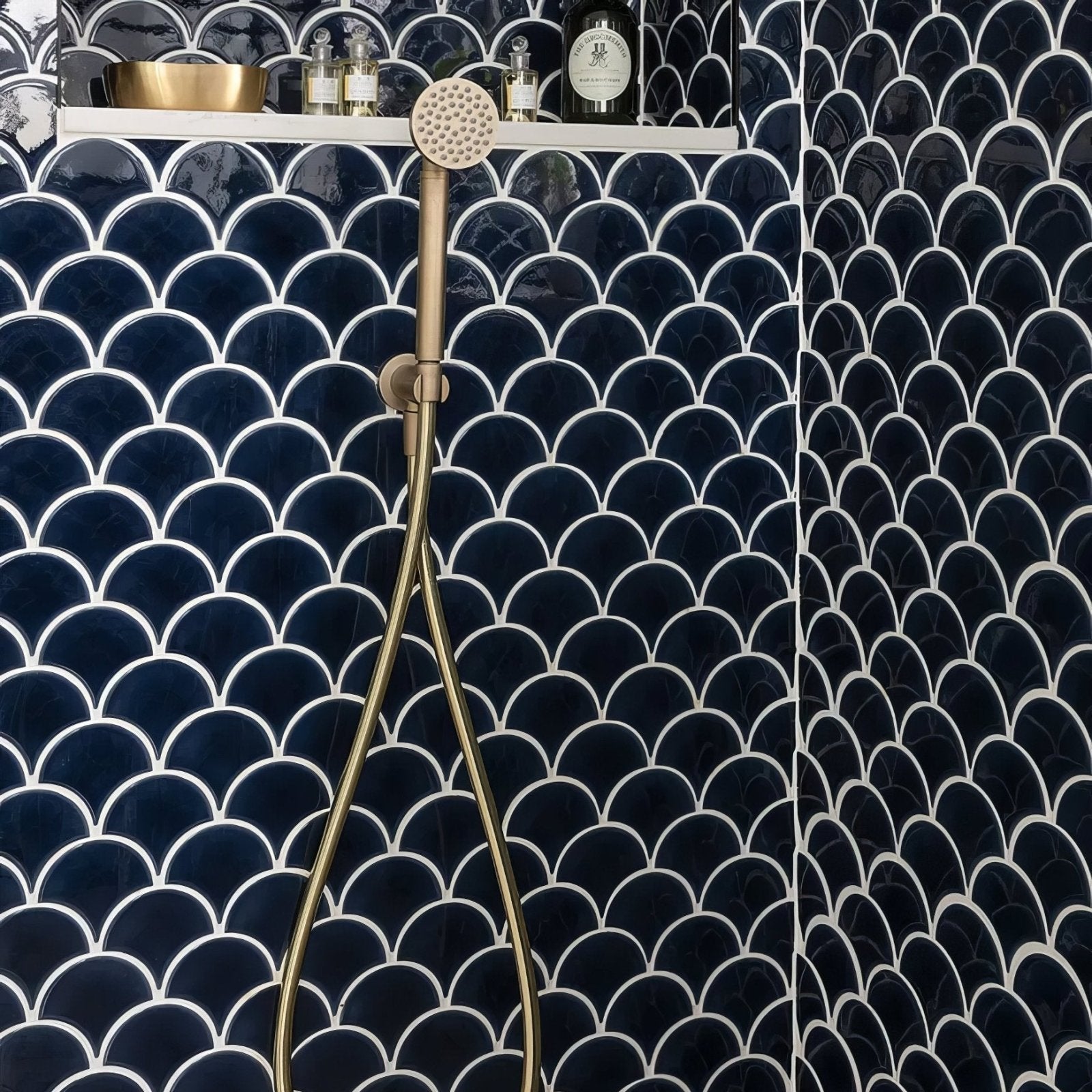 Brass showerhead with perforated circular head and slender hose against dark blue Atlantis porcelain mosaic navy tiles
