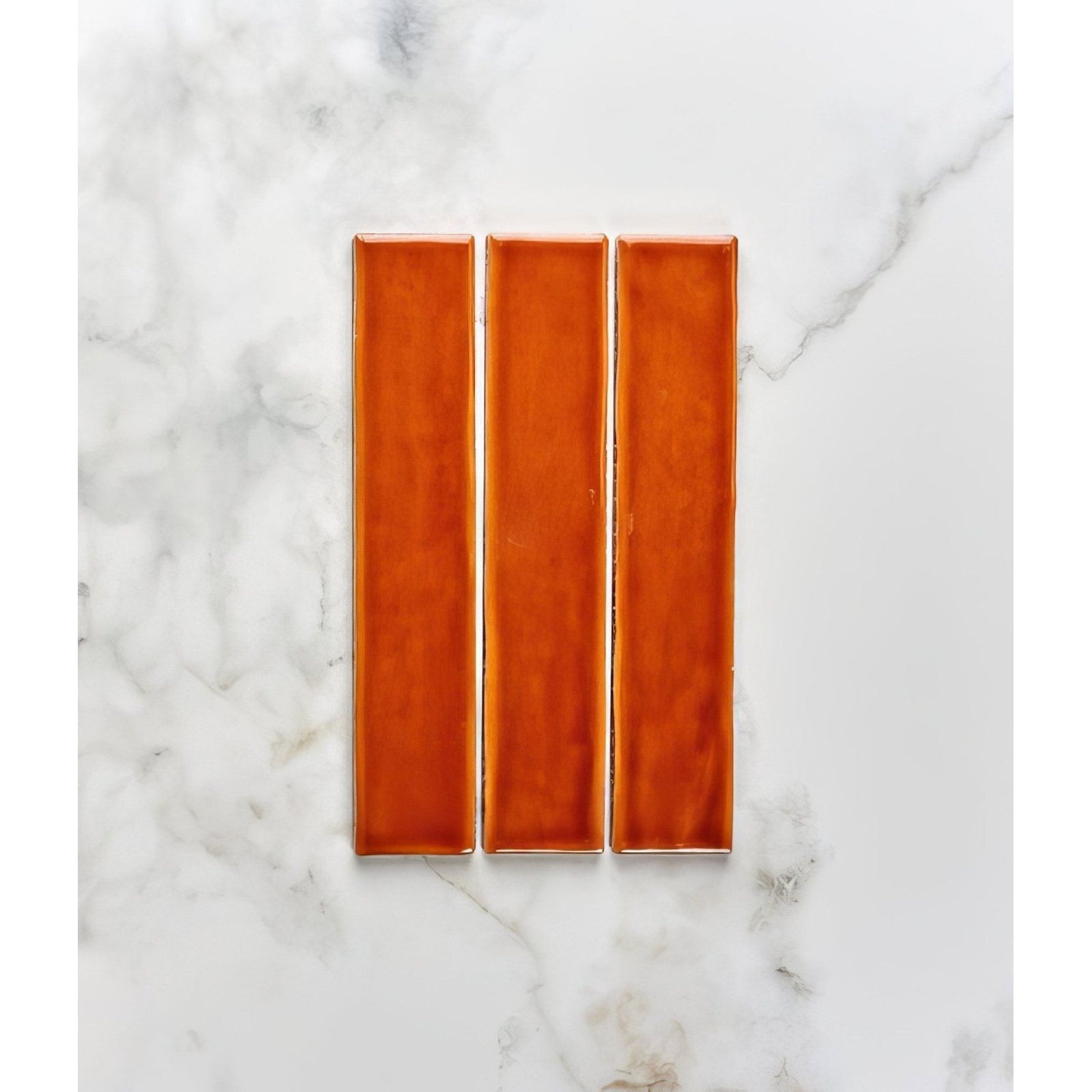 Three rectangular glossy burnt caramel ceramic tiles from avebury arranged vertically on a marble surface