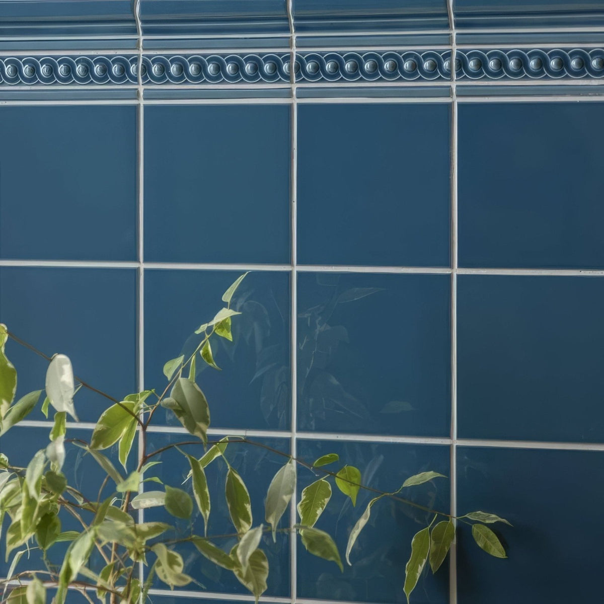 Deep blue ceramic baroque blue field tile with decorative beaded border white grout and green foliage accents