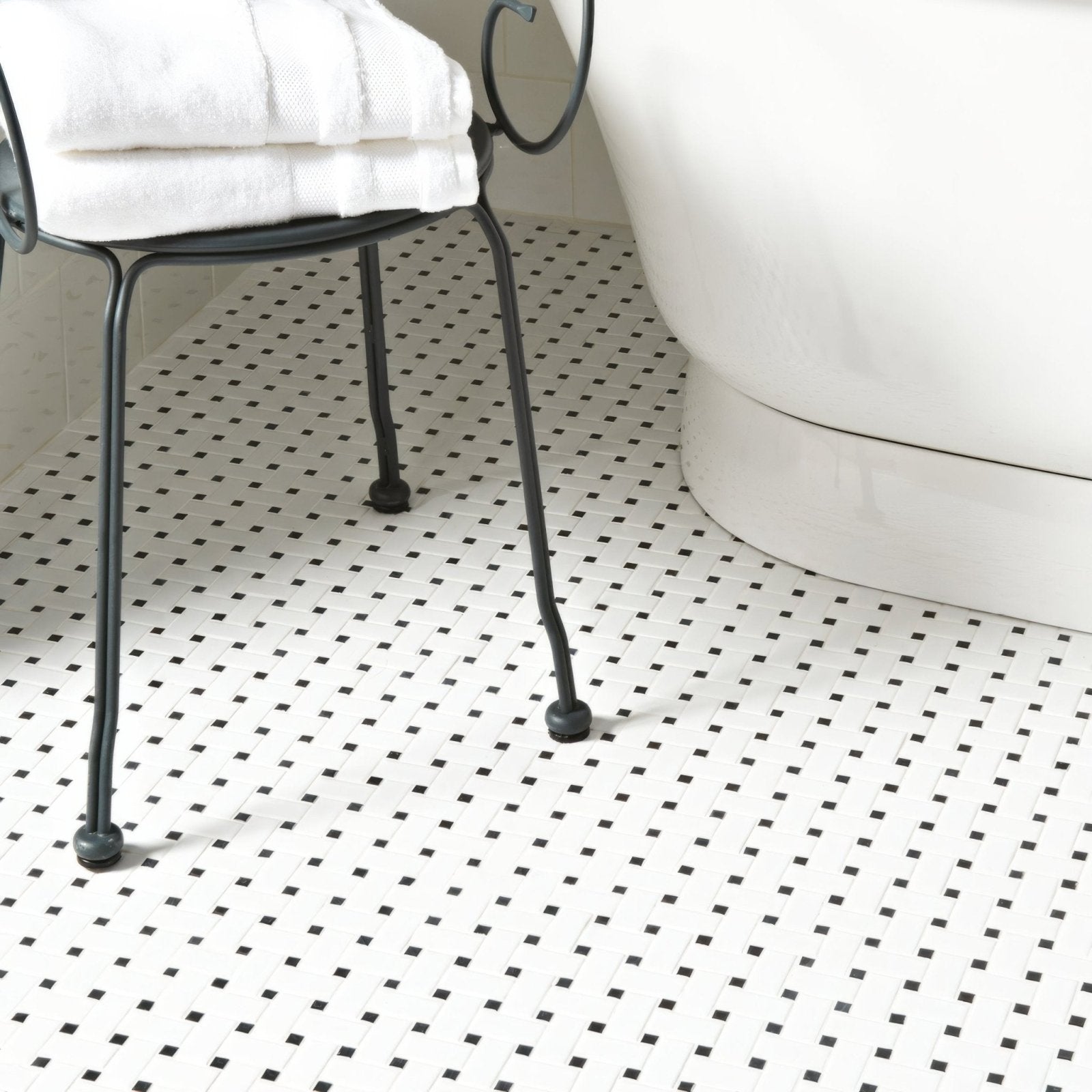 Black metal chair with curved legs and white towel draped over seat in basketweave floor mosaic setting