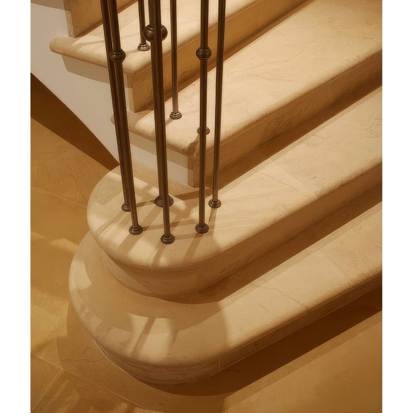 Bronze-finished metal balusters with spherical accents lining a curved cream-colored bath limestone artisan honed finish staircase
