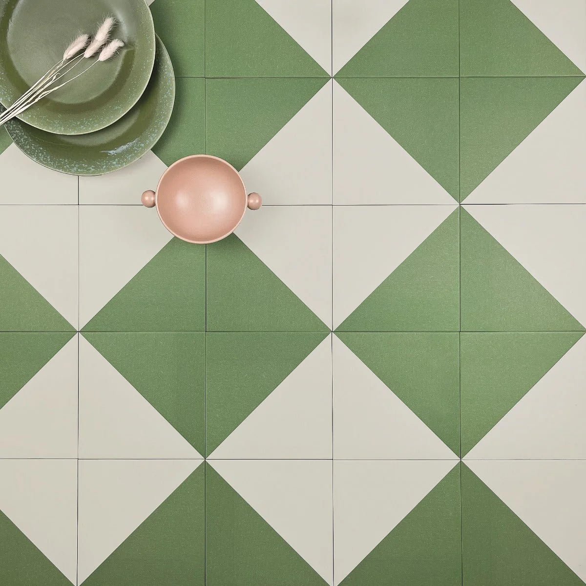 A blush pink ceramic bowl with rounded handles on a geometric green and white tiled surface from bert & may