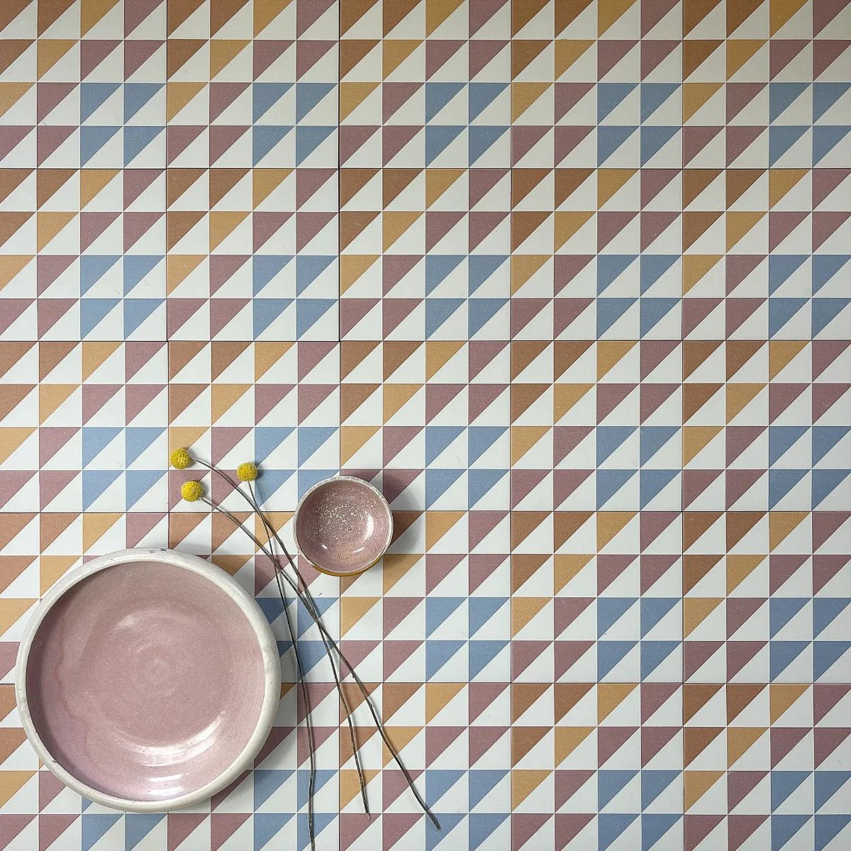 A matte-finished blush pink ceramic bowl with a white rim on bert and may soho majadas geometric porcelain tile floor